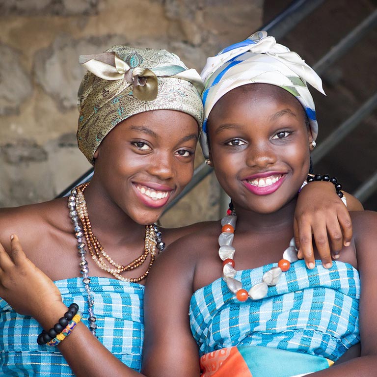 Two African women wearing bright dresses smiling at camera